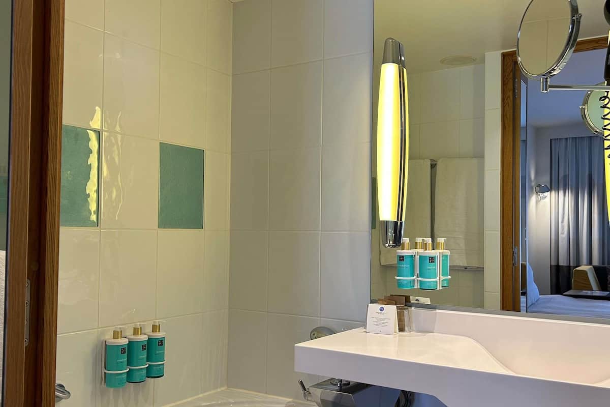 A bathroom with a white sink, a mirror, and a bathtub. There are toiletries on the wall and a towel rack.