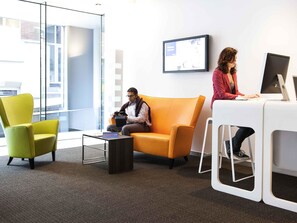 A modern office space with a glass wall, a yellow sofa, a green armchair, and a white desk with a computer. - Novotel Mechelen Centrum (Mechelen)