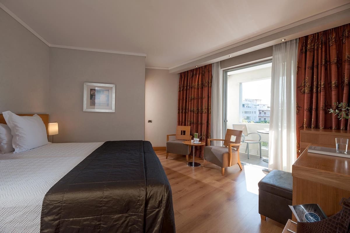 A hotel room with a bed, a desk, a chair, and a view of the city.