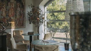 A room with a round glass table, beige chairs, a large window with a view, and a hanging light fixture. - Athenian Callirhoe Hotel (Athens)