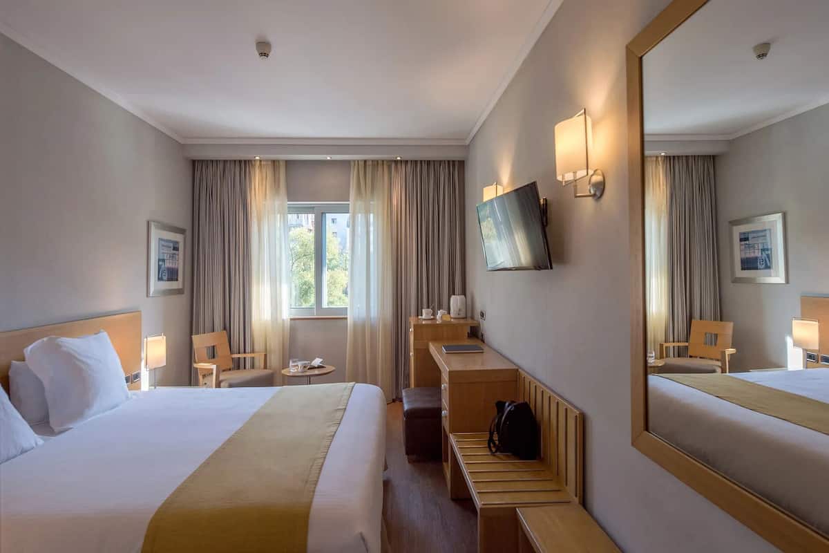 A hotel room with a bed, a desk, a chair, a TV, and a large mirror.