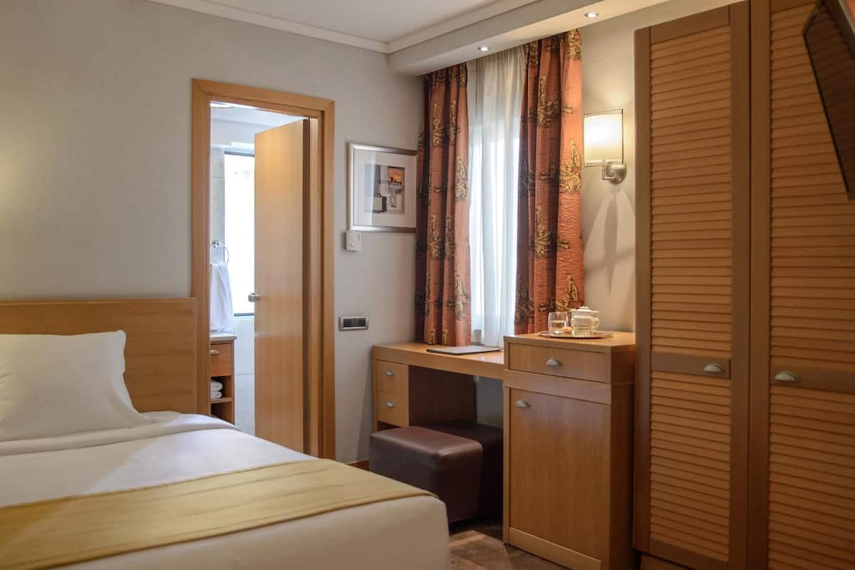 A hotel room with a bed, a desk, a wardrobe, and a window with curtains.