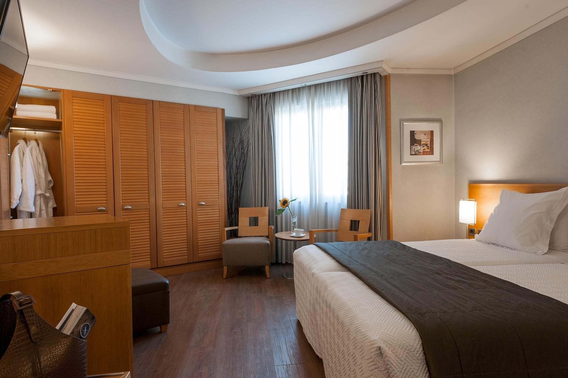 Una habitación de hotel con cama, escritorio, silla, armario y ventana con cortinas.