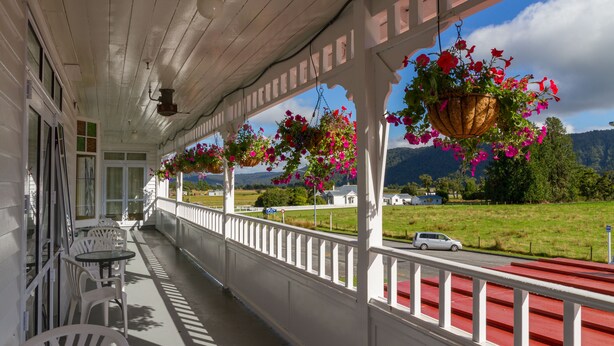 A covered porch with white railings, hanging flower baskets, and outdoor seating. - Heartland Hotel Fox Glacier (Fox Glacier)