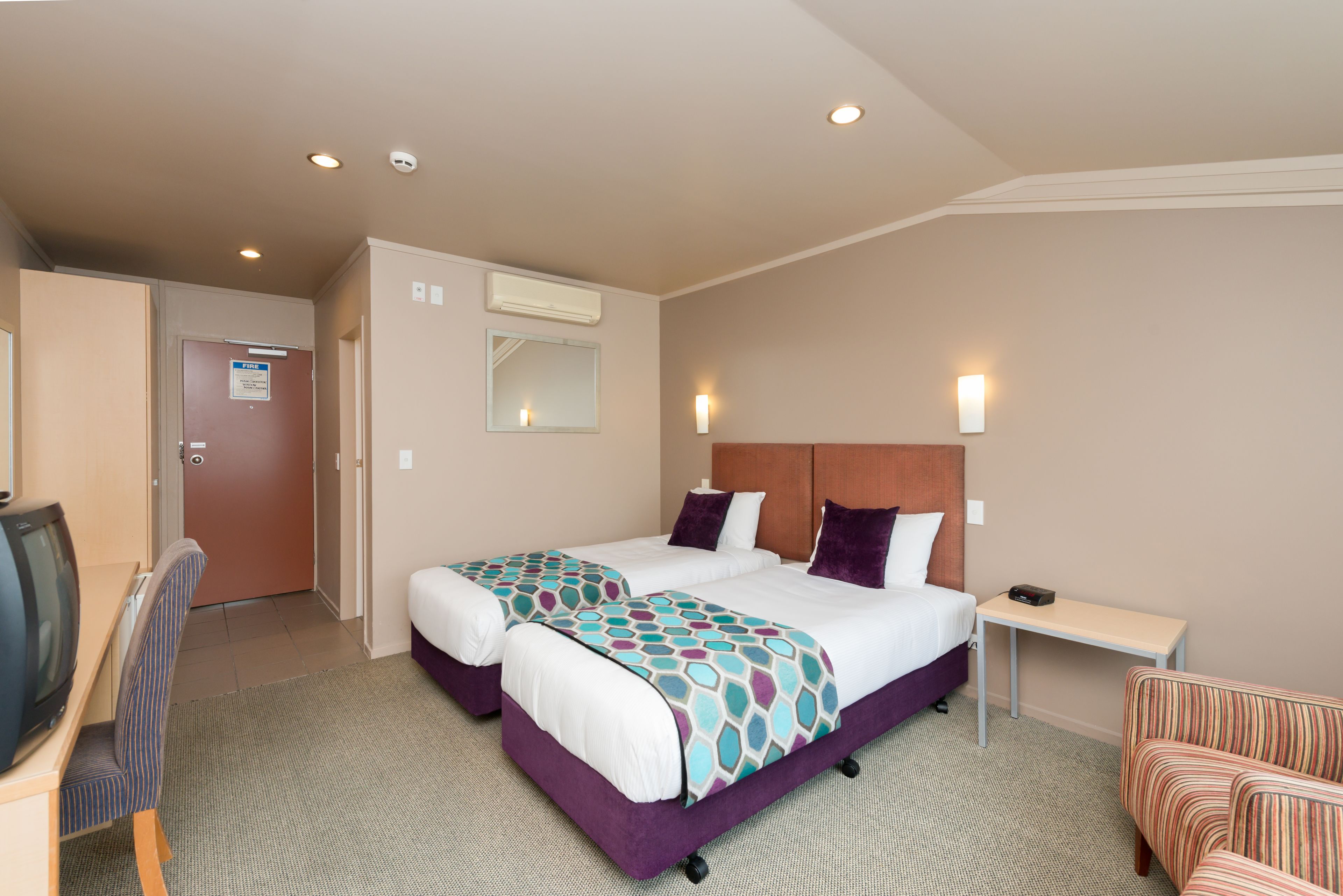 A hotel room with two beds, a desk, a chair, a TV, and a couch.
