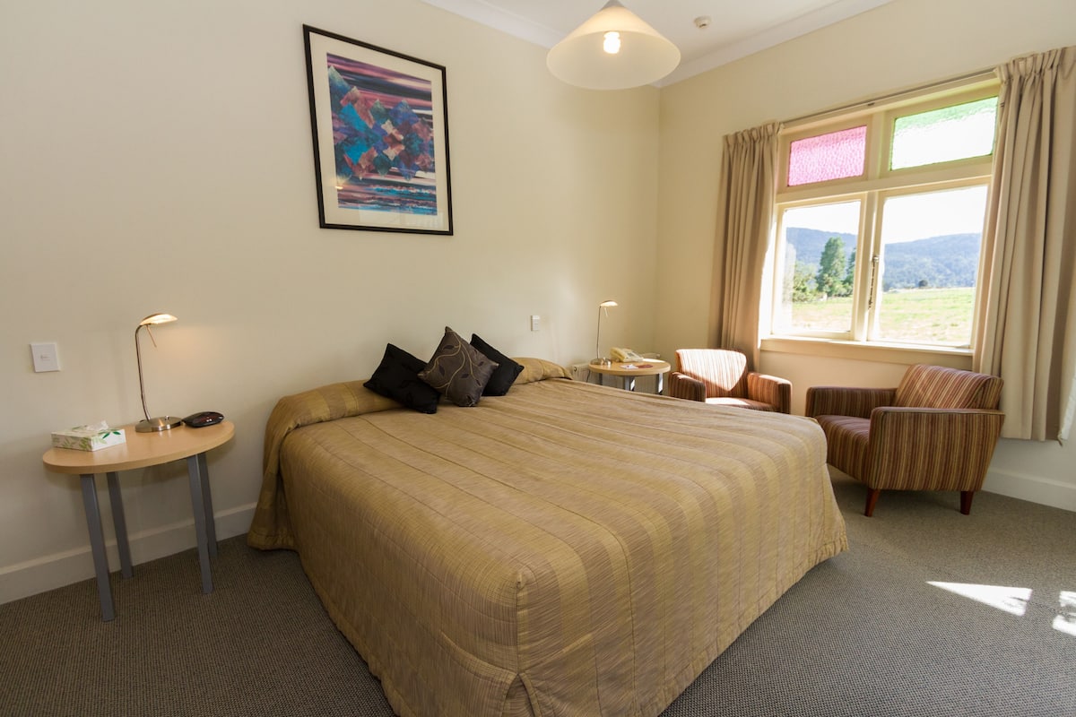 Ein Hotelzimmer mit einem großen Bett, einem Schreibtisch, einem Stuhl und einem Fenster mit Blick ins Freie.