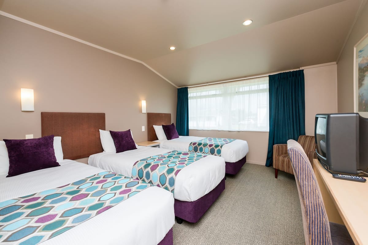 Ein Hotelzimmer mit drei Betten, einem Fernseher und einem Schreibtisch.