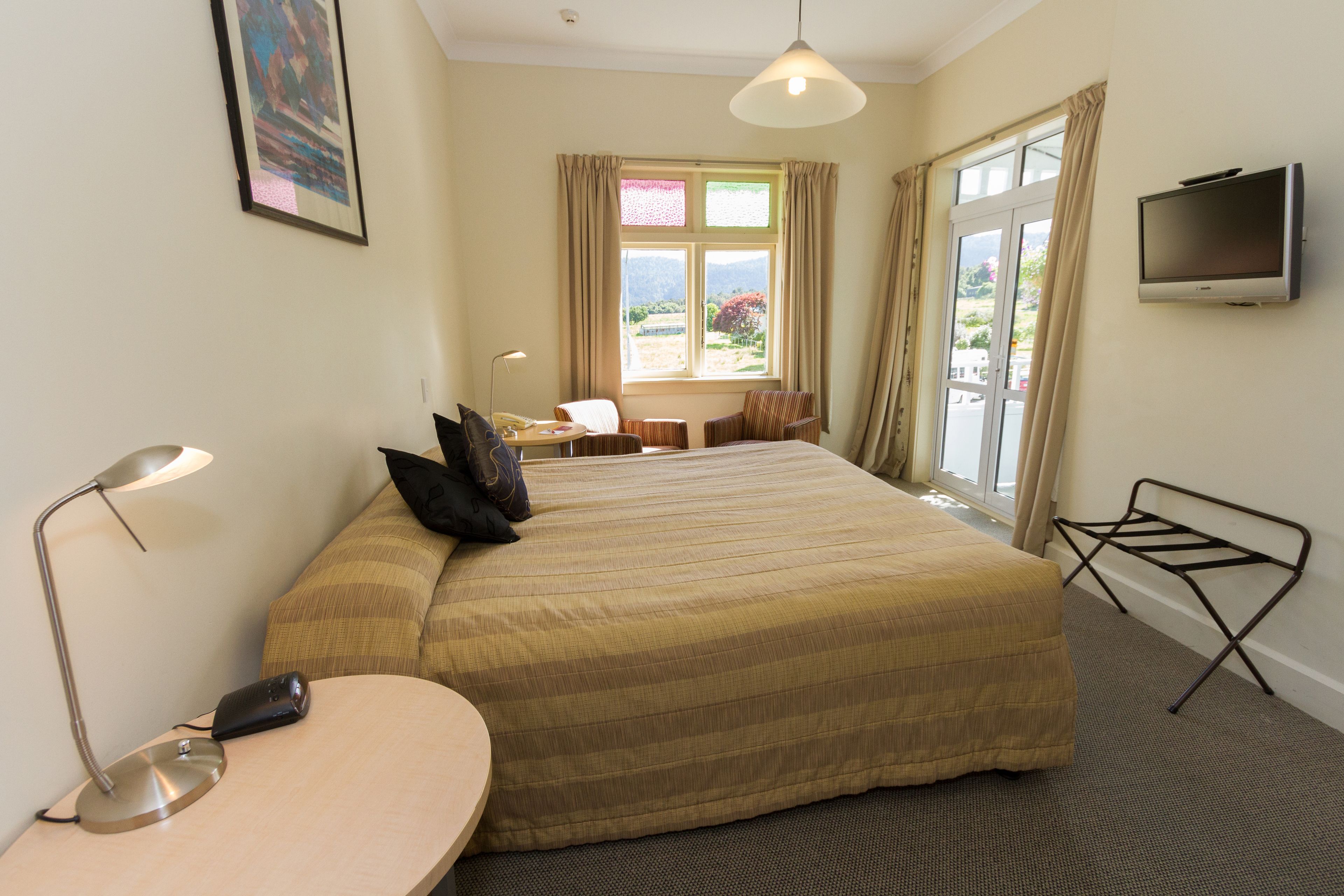 Une chambre d’hôtel avec un grand lit, un bureau avec une lampe, une télévision et une vue sur l’extérieur.