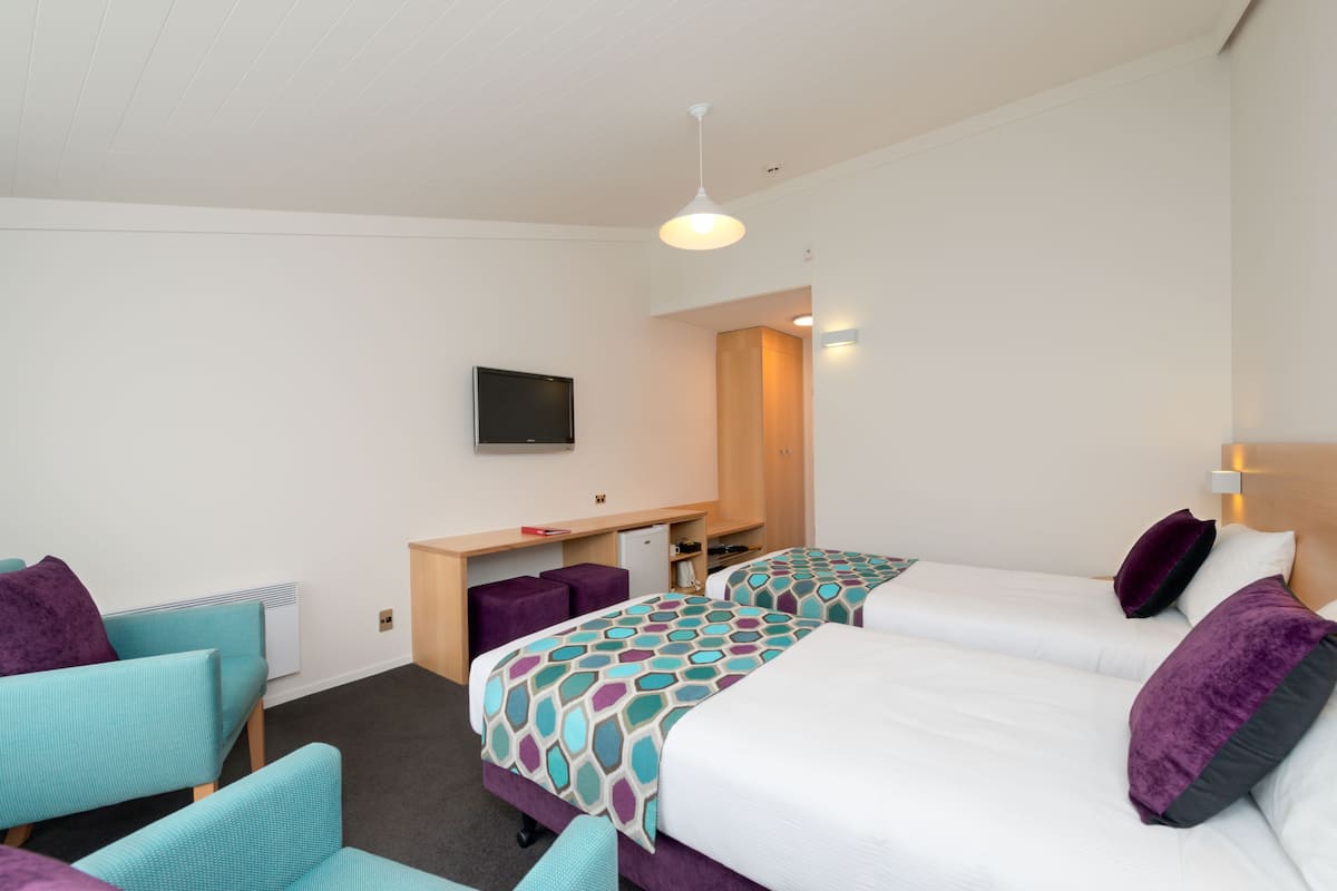 Ein Hotelzimmer mit zwei Betten, einem Schreibtisch, einem Fernseher und einer Sitzecke mit Sesseln.
