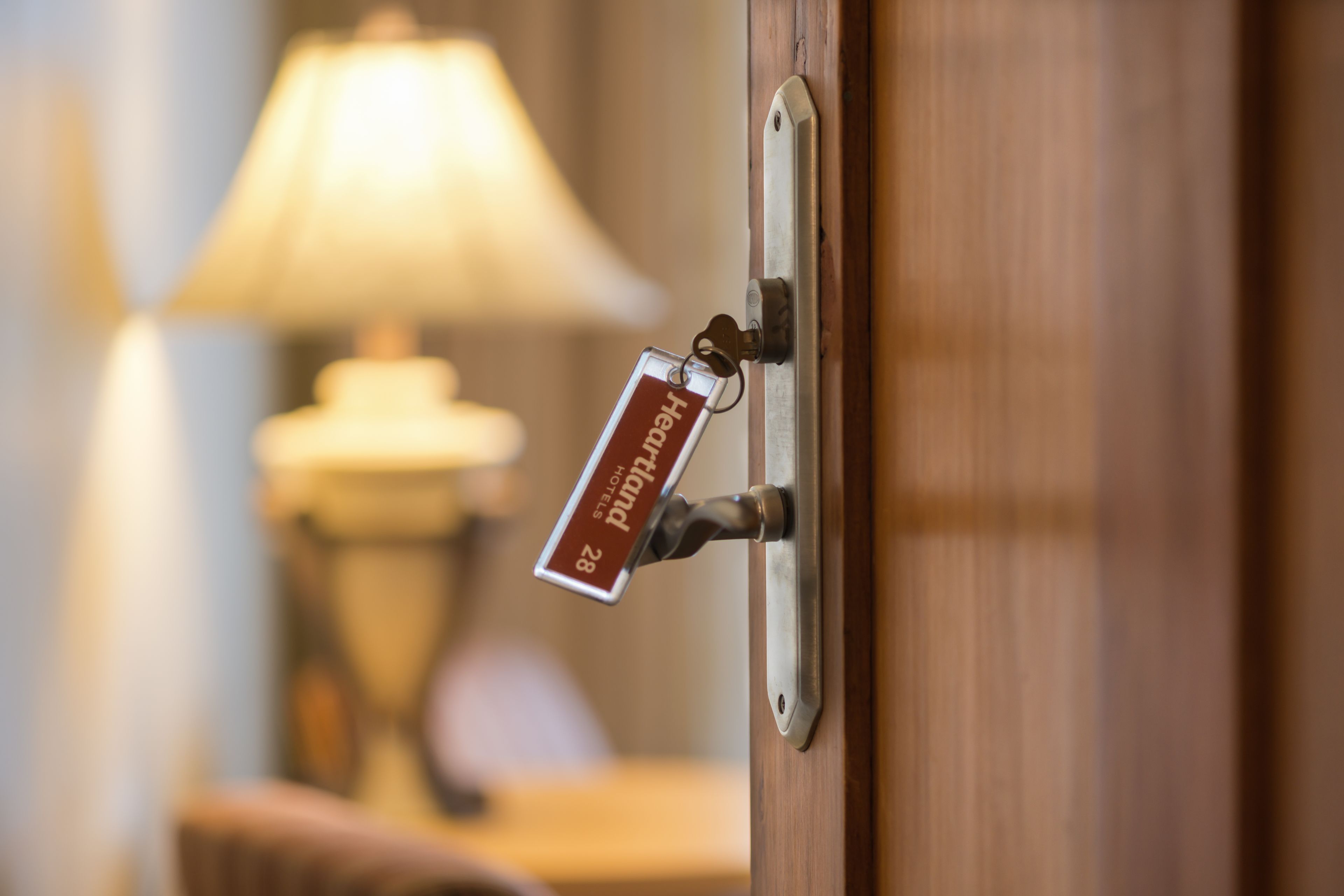 A hotel room door with a keycard holder displaying "Hotel 28" and a lamp in the background.
