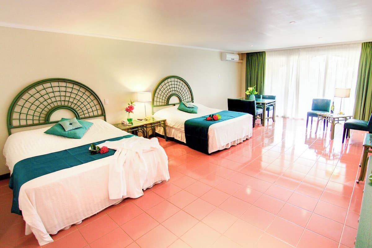 A hotel room with two beds, a small table, chairs, and a window with curtains.