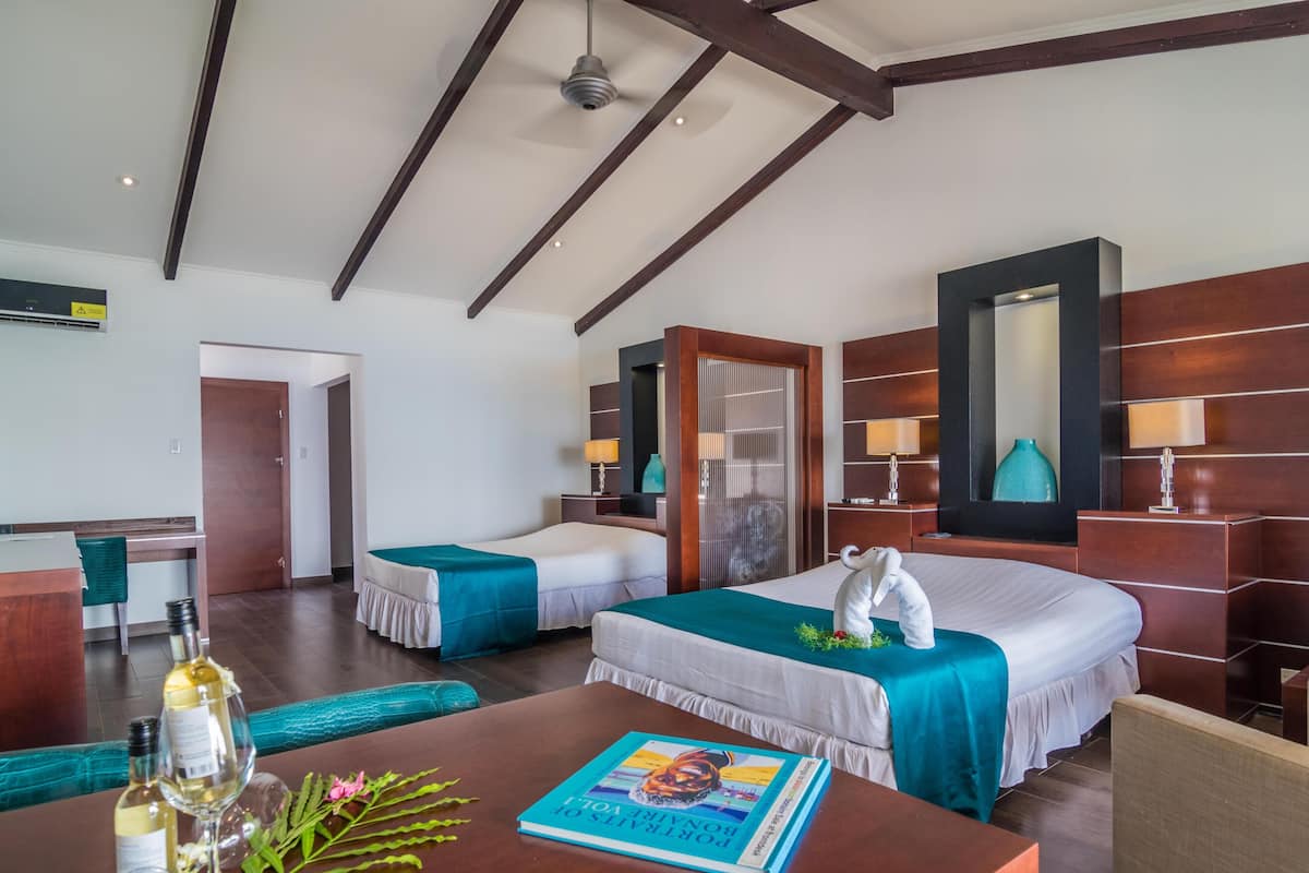 A hotel room with two beds, a desk with a book and wine glasses, a mirror, and a door.