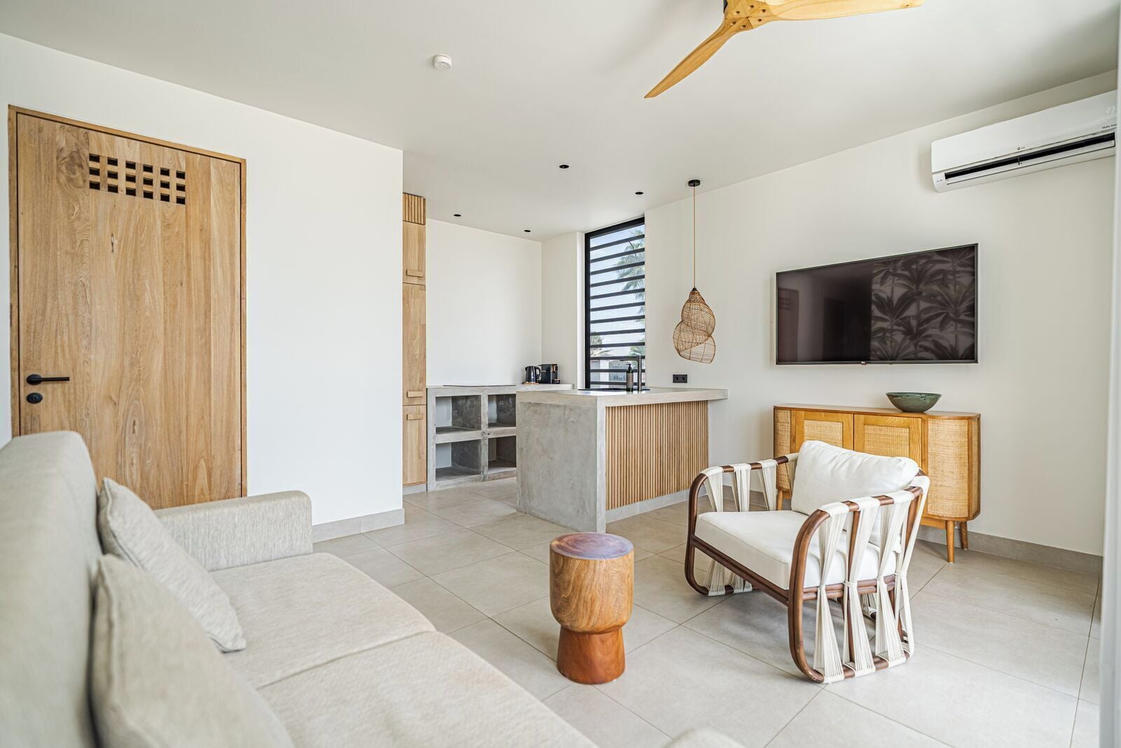 Una sala de estar moderna con un sofá, una silla de madera, una mesa redonda de madera y una zona de cocina con barra.
