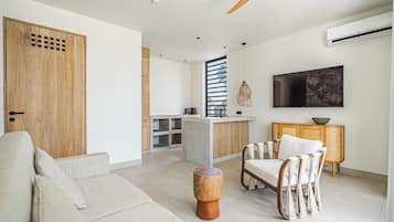 Una sala de estar moderna con un sofá, una silla de madera, una mesa redonda de madera y una zona de cocina con barra.