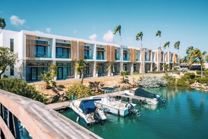 A modern hotel with a poolside area, multiple boats, and palm trees. - Van der Valk Plaza Beach & Dive Resort Bonaire - All Inclusive (Kralendijk)