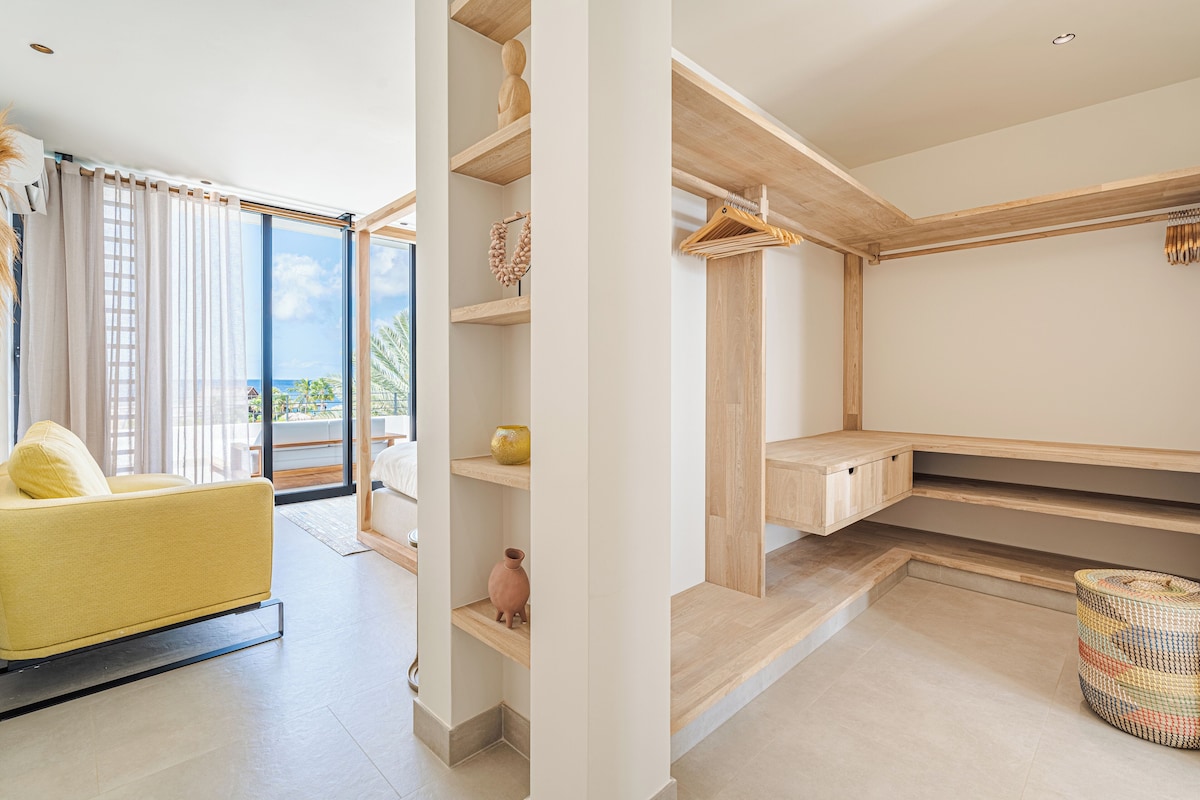 A modern living room with a yellow sofa, wooden shelves, and a view of the outdoors.