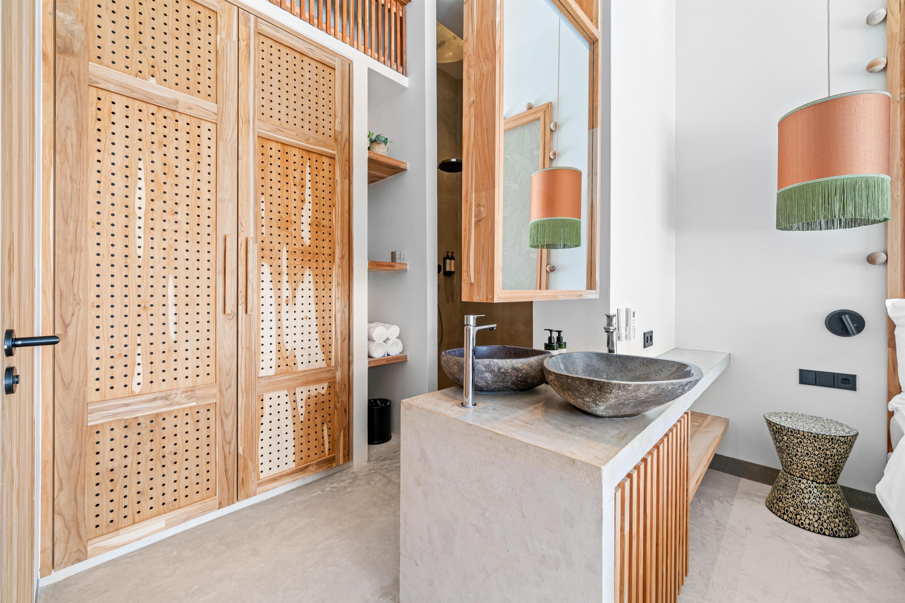 A modern bathroom with wooden cabinets, a large mirror, two stone sinks, and a hanging light fixture.