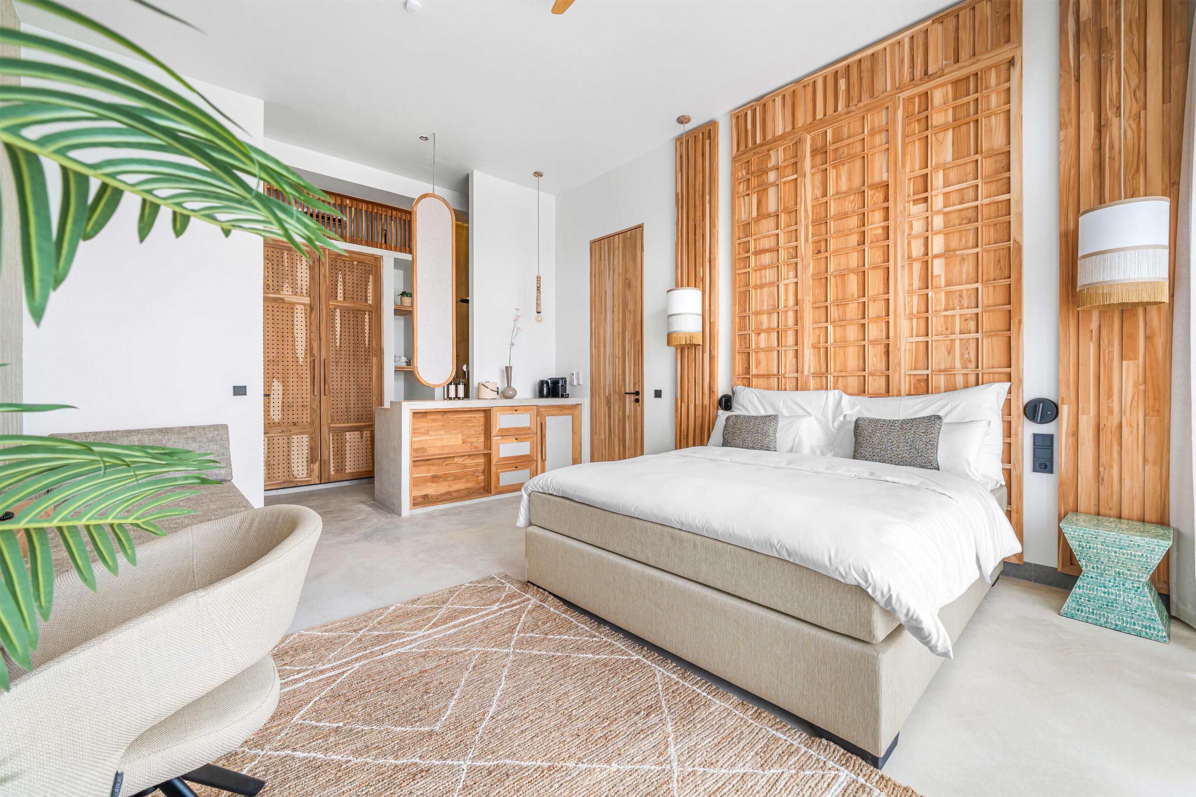 A bedroom with a large bed, a wooden headboard, a bedside table, a chair, and a large mirror.