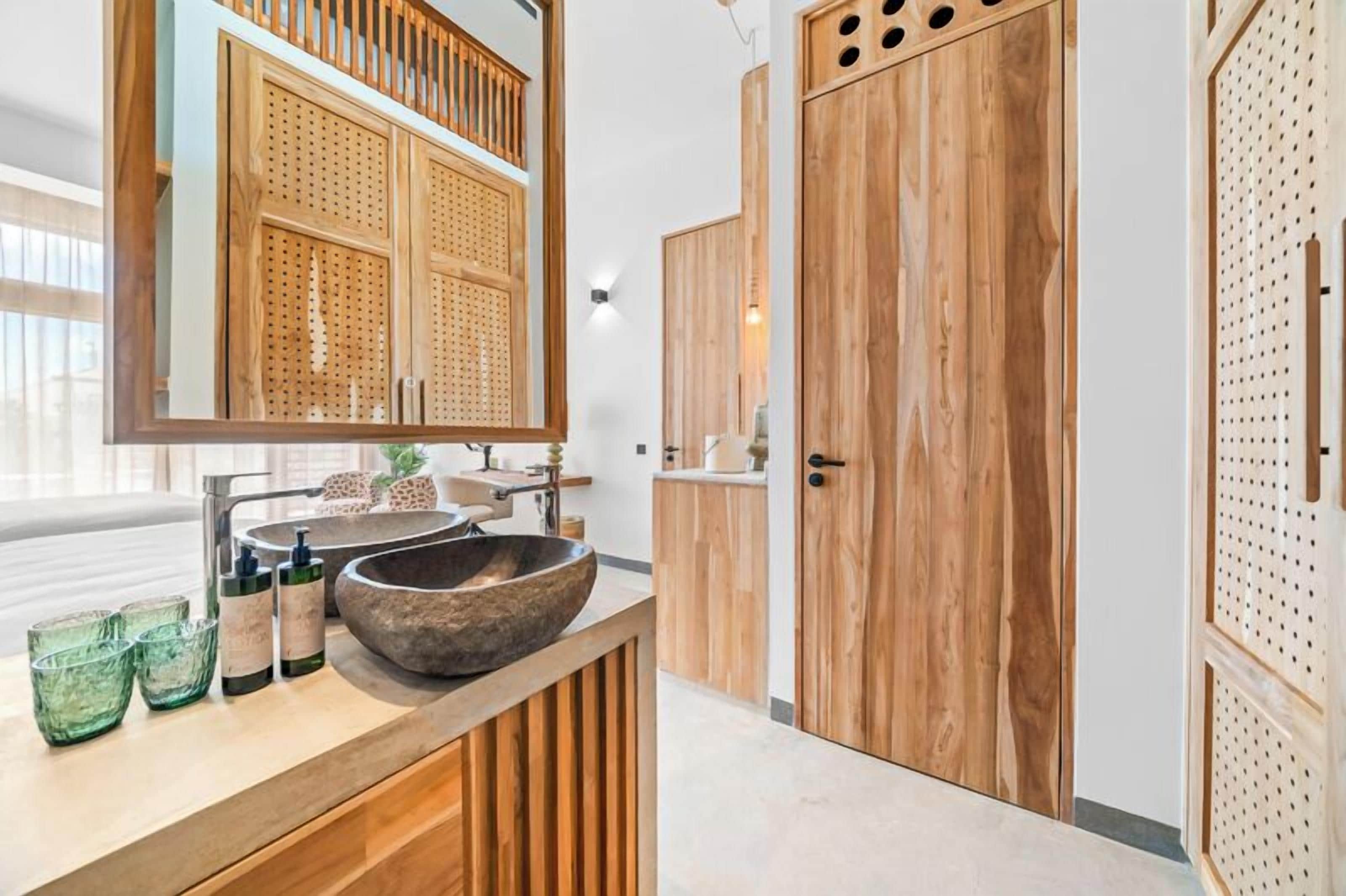 Un baño moderno con un mueble de tocador grande de madera, un lavabo de piedra y un espejo grande.
