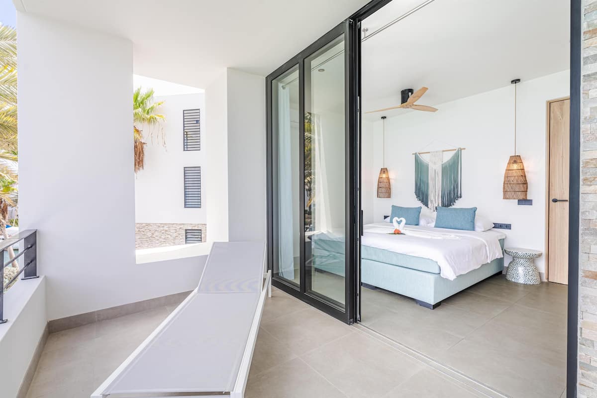 A modern bedroom with a bed, a glass door leading to a balcony, and a small table.