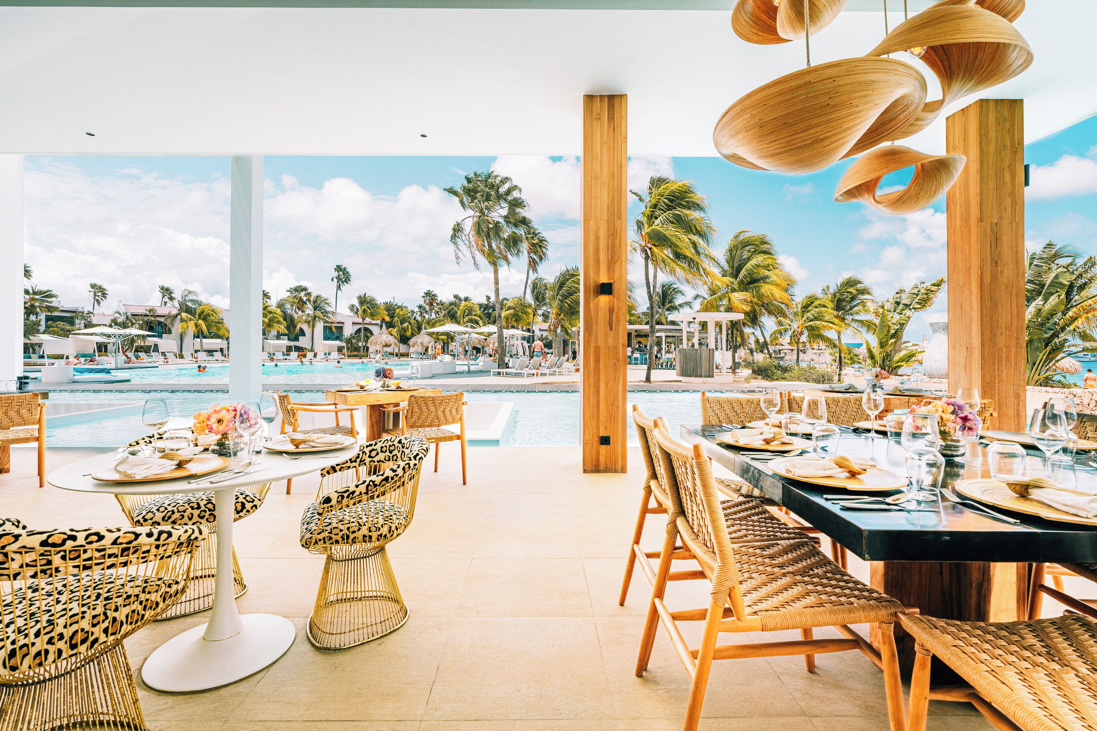 A dining area with a pool view, wicker furniture, and a tropical setting.