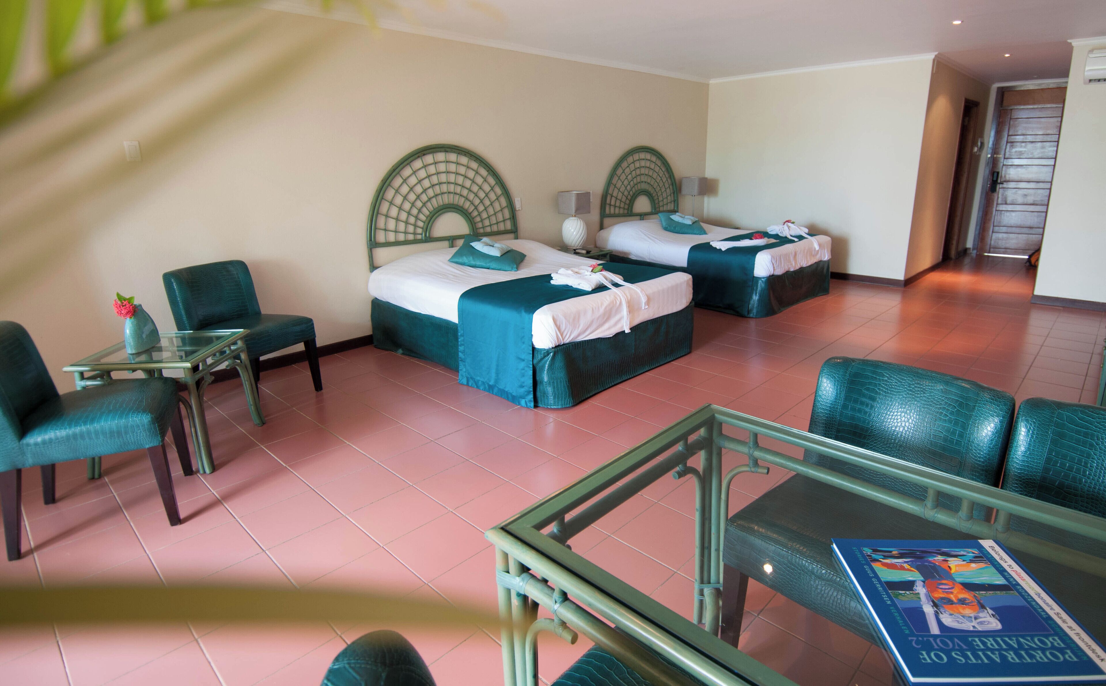 A hotel room with two single beds, a small table with a vase, and a glass table with a book.