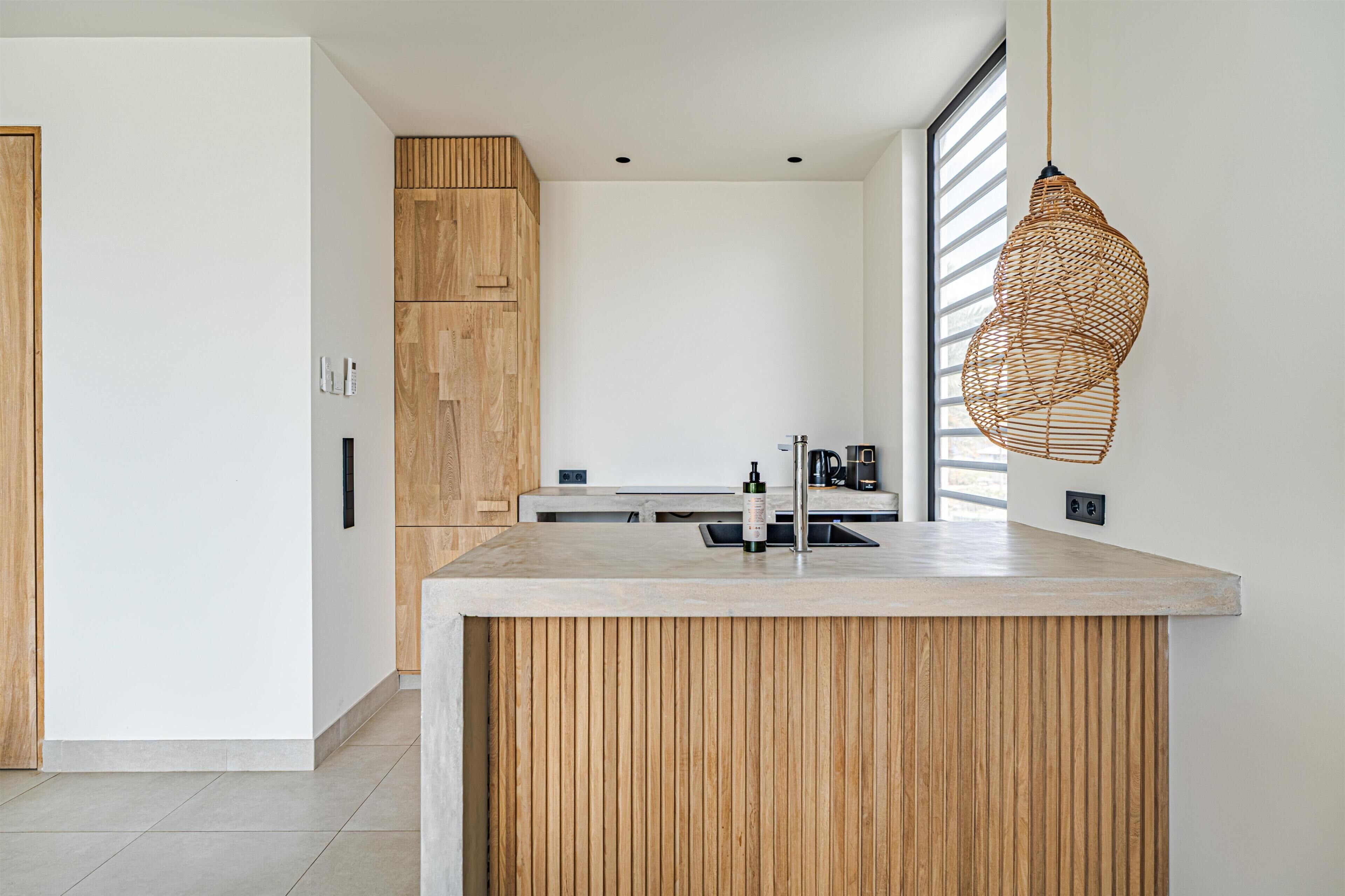 A modern kitchen with a wooden island, a hanging light fixture, and a large window.