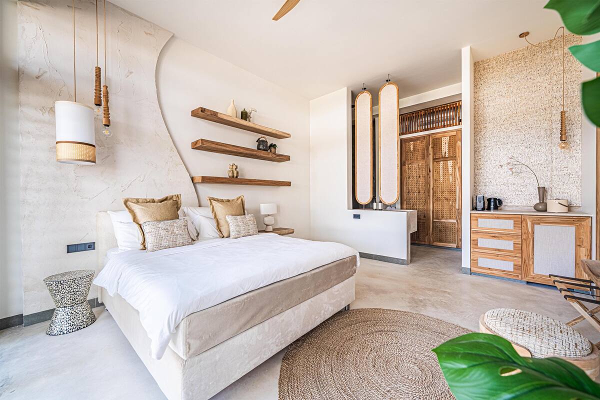A modern bedroom with a large bed, bedside tables, a bedside lamp, a wooden dresser, and a mirror.