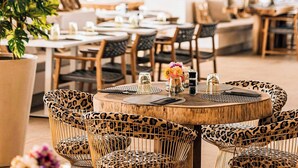 A restaurant with round tables, wicker chairs, and hanging wooden light fixtures.