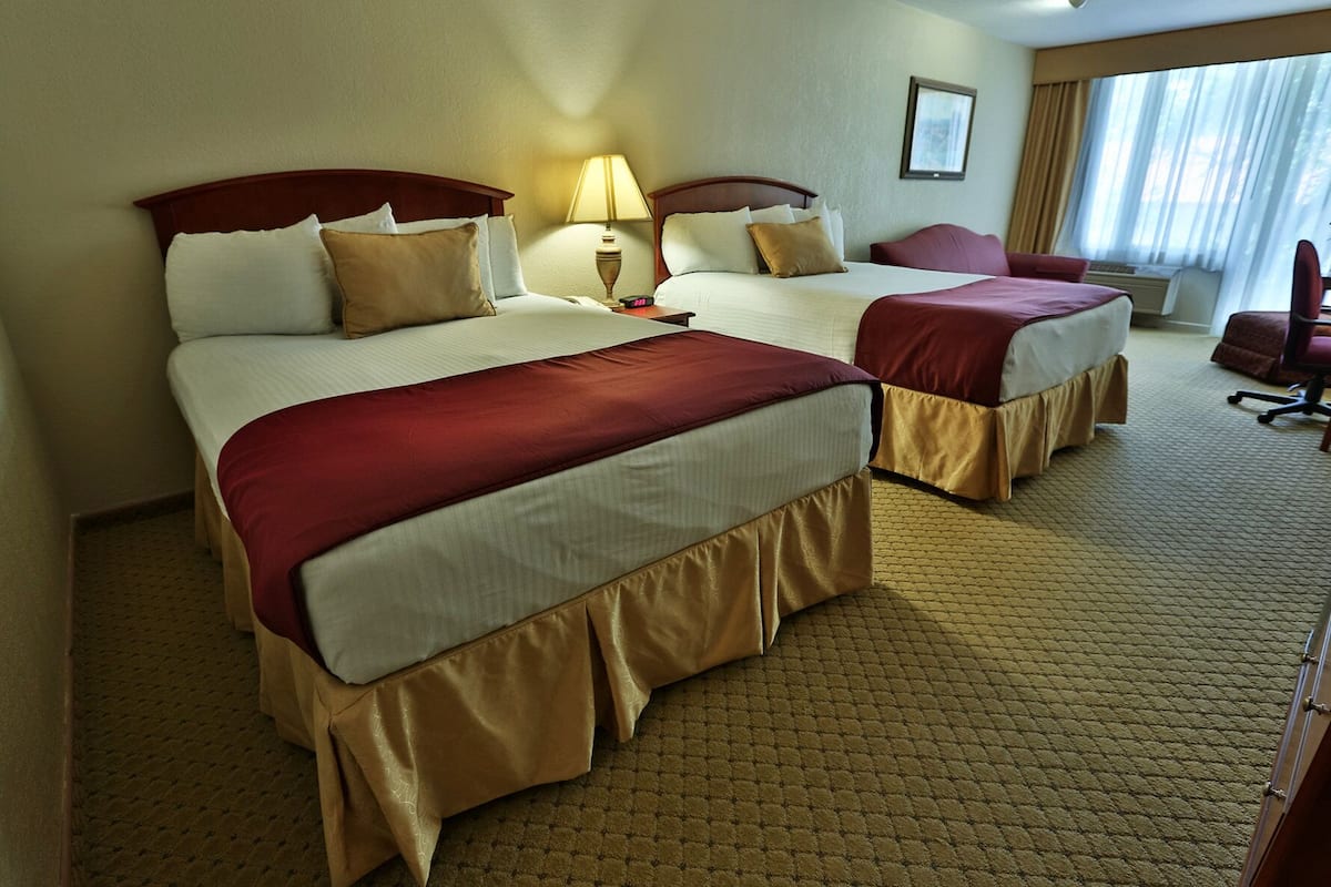 A hotel room with two beds, a desk, a chair, and a window with curtains.
