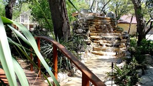 A stone water feature with cascading water, surrounded by greenery and trees. - The Inn Of The Hills (Kerrville)