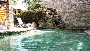A clear pool with rocks, a stone wall, and a lifeguard sign. - The Inn Of The Hills (Kerrville)