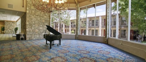 Una habitación amplia con un piano de cola, una alfombra estampada y grandes ventanales que ofrecen vistas al exterior del edificio.