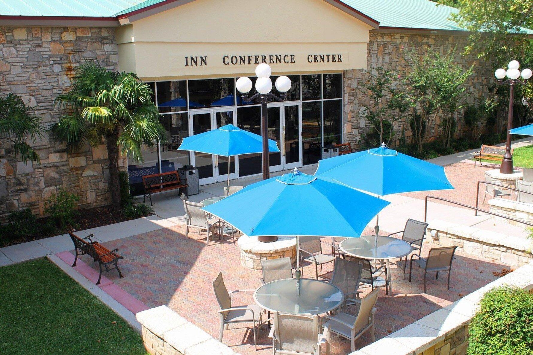 An outdoor seating area with tables and chairs, blue umbrellas, and a stone building labeled "INN CONFERENCE CENTER".