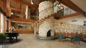 A spacious lobby with a stone fireplace, a grand piano, and a high-ceilinged wooden staircase. - The Inn Of The Hills (Kerrville)