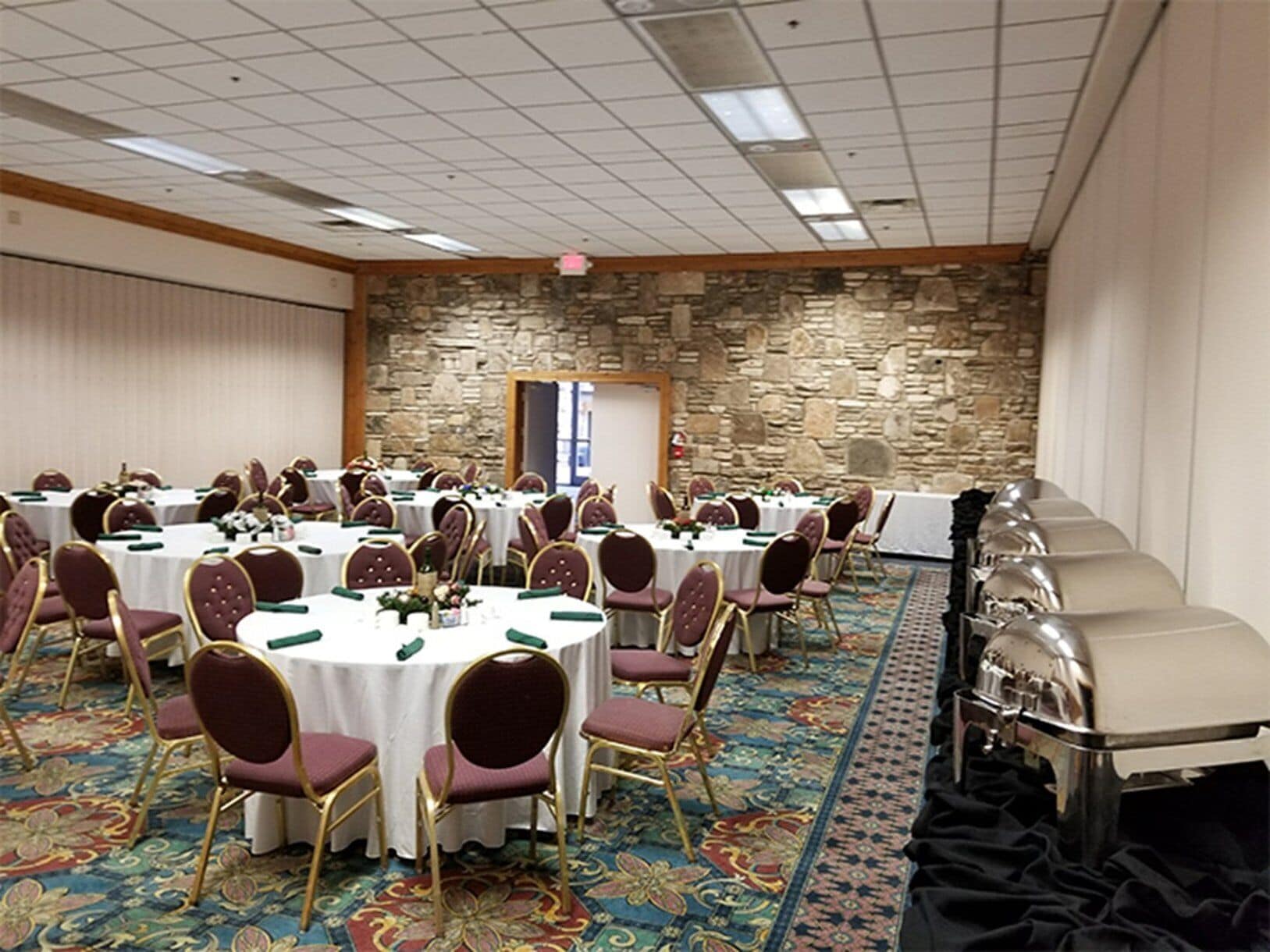 Salão de banquetes com mesas redondas, cadeiras e mesa de buffet.