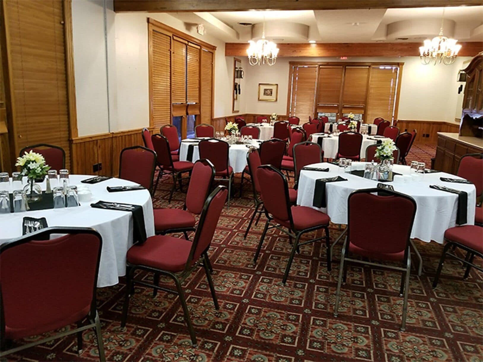 Une salle de banquet avec des tables rondes, des chaises rouges et un tapis à motifs.