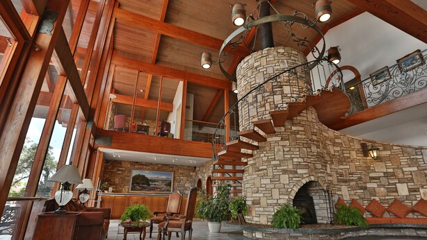 A spacious lobby with a stone fireplace, wooden beams, and a high ceiling. - The Inn Of The Hills (Kerrville)