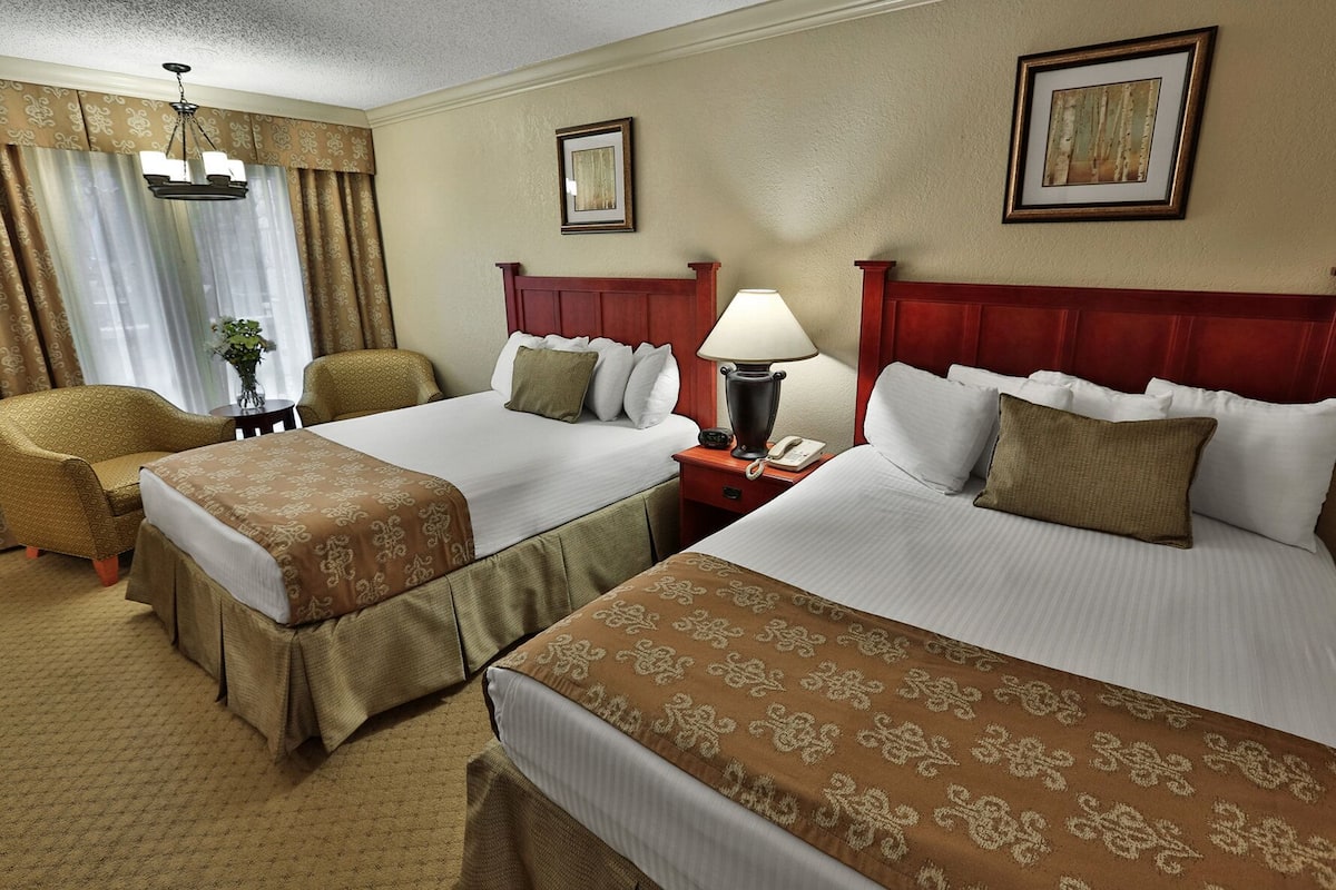 A hotel room with two beds, a sitting area with a chair, a lamp, and a small table.