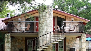 A two-story stone house with a balcony, a staircase, and a front door. - The Inn Of The Hills (Kerrville)
