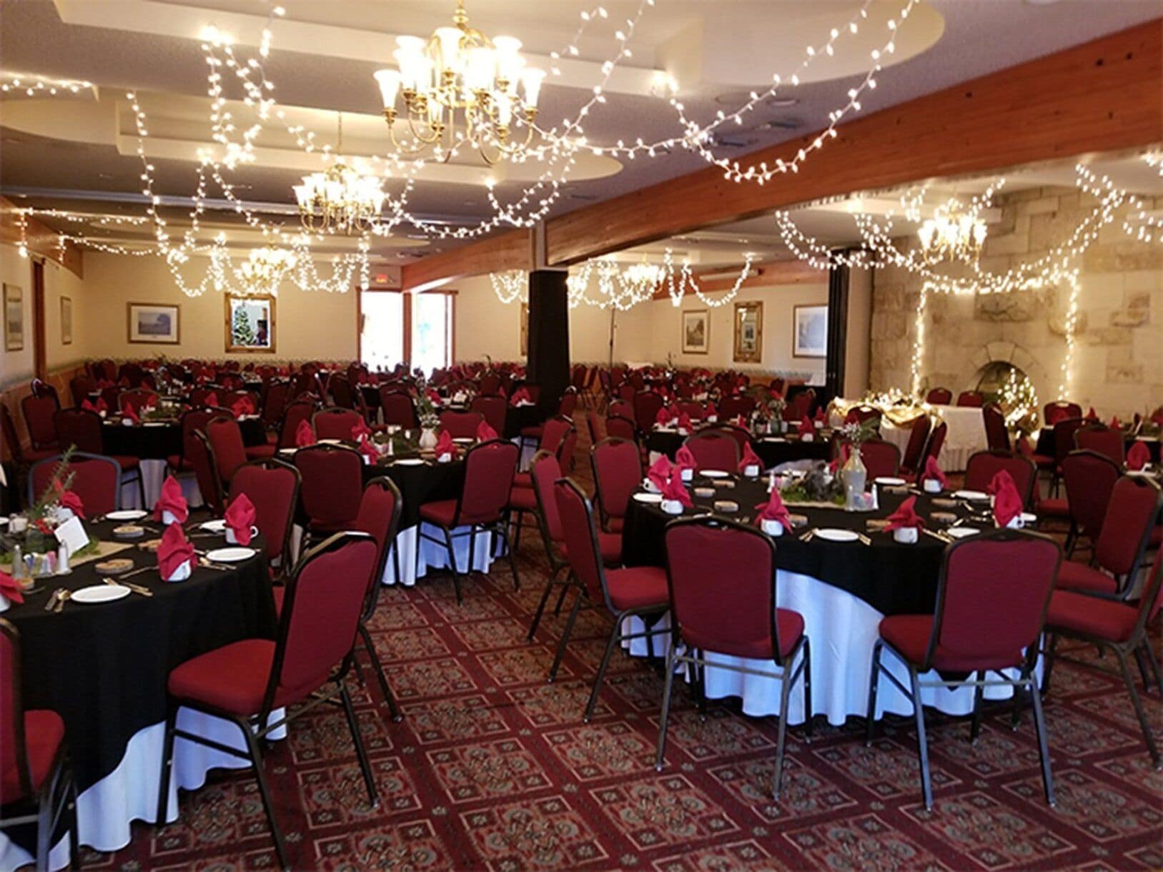 A banquet hall with round tables, red chairs, chandeliers, and string lights.