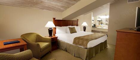 A hotel room with a bed, two bedside lamps, a wooden nightstand, a patterned armchair, and a desk with a lamp.