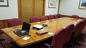 A conference room with a wooden table, red chairs, a laptop, a projector, and a whiteboard.