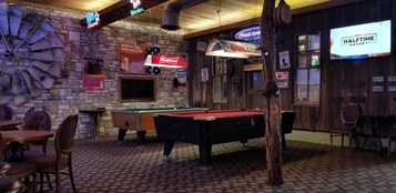 Een pooltafel in een bar met een rustieke stenen muur en neonreclames voor Bud Light, Coors Light en Heineken.