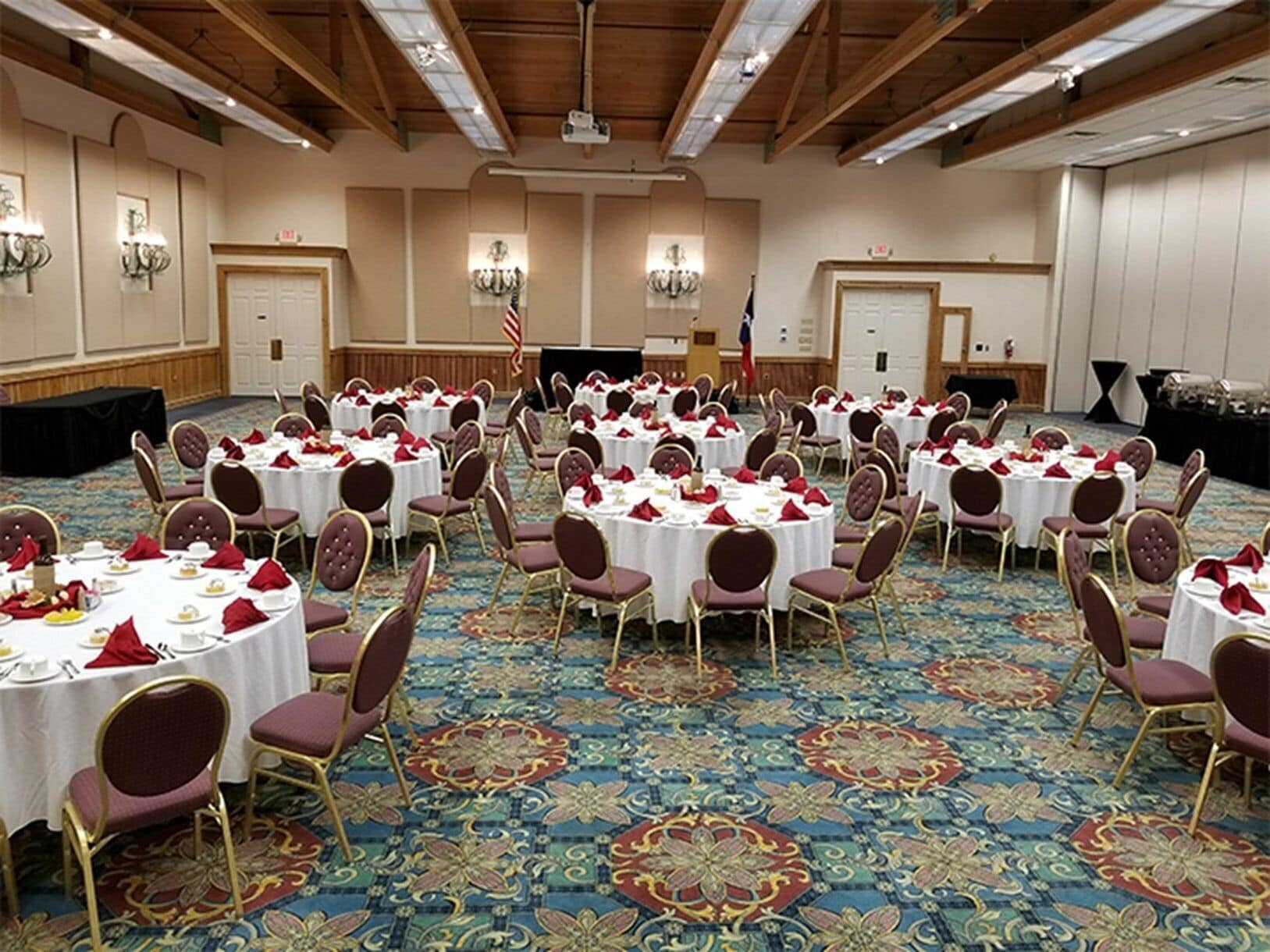 A banquet hall with round tables, red and gold chairs, and a patterned carpet.