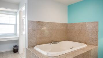 A modern bathroom with a freestanding bathtub, granite countertops, and a window with blinds.