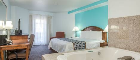 A hotel room with a bed, desk, chair, and a large bathtub.