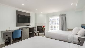Quarto de hotel com duas camas, uma escrivaninha com cadeira, televisão de tela plana na parede, lareira e janela com cortinas.