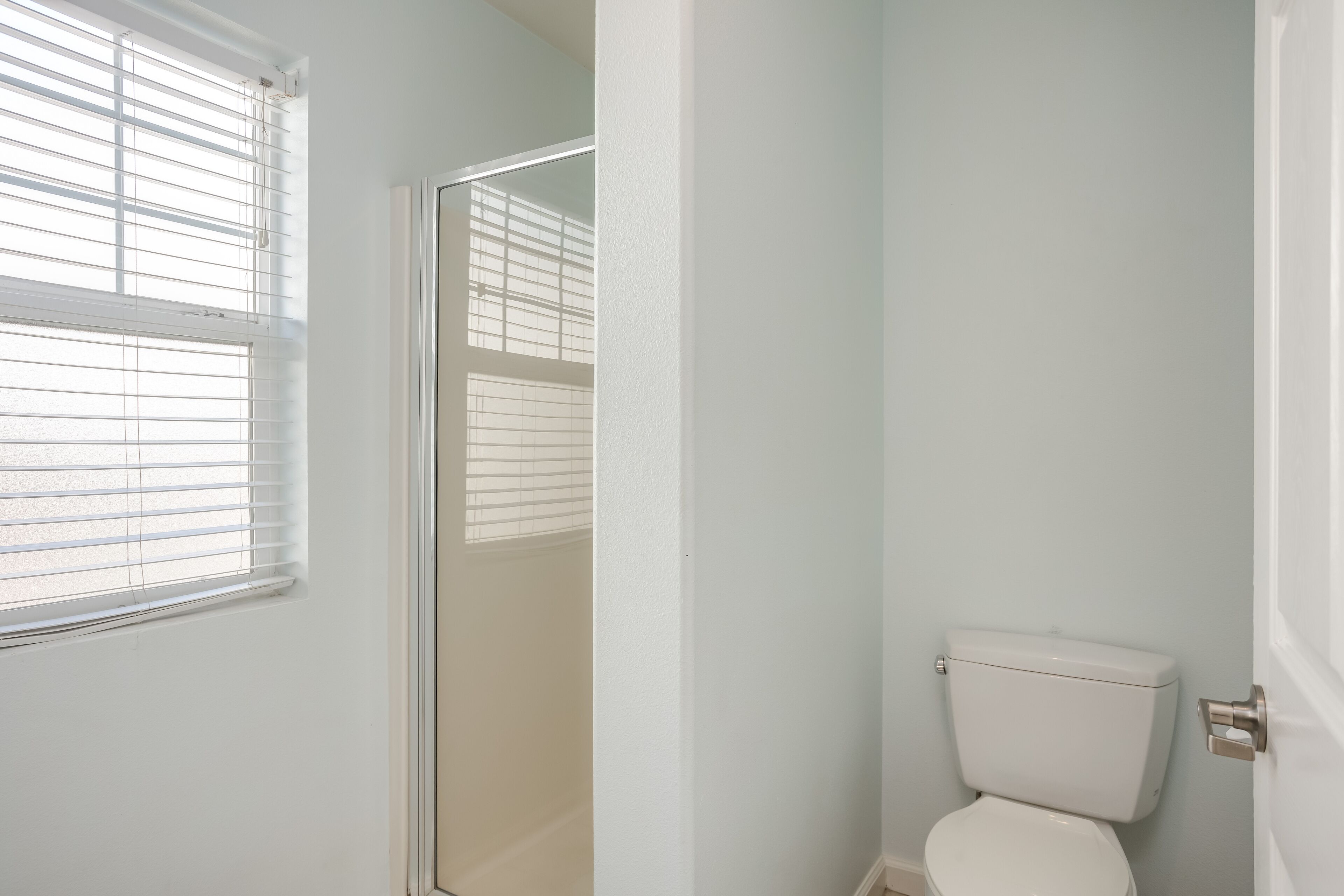 Un baño con inodoro, ventana con persianas y puerta.