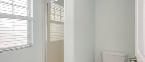 A bathroom with a toilet, a window with blinds, and a door.